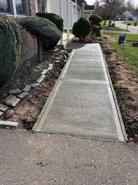 Newly poured concrete sidewalk with a dirt border, next to lawn and shrubbery.