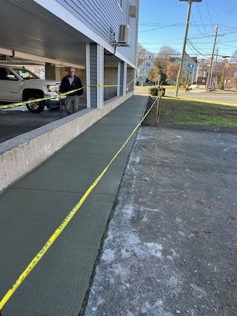 New concrete ramp with yellow caution tape; man standing at the top of the ramp; beside building.