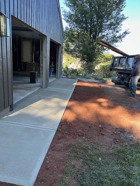 Exterior view of a building with a new concrete walkway; a truck dumps soil nearby.