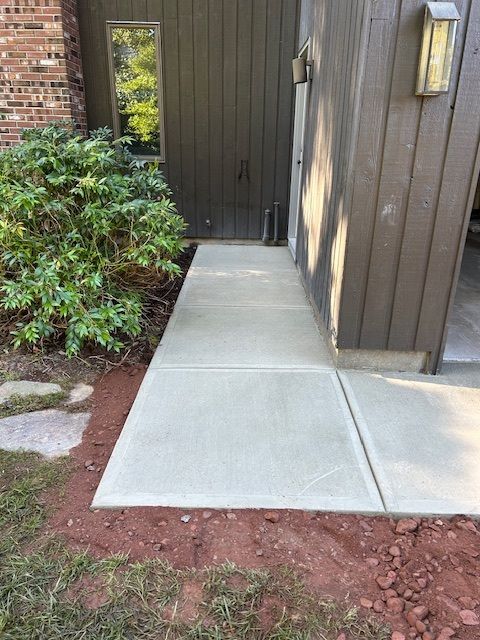 New concrete sidewalk next to a brown building. Freshly poured concrete, edged with dirt and grass.
