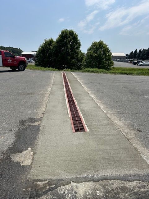 Concrete area with red grate drainage, trees, and a red truck.