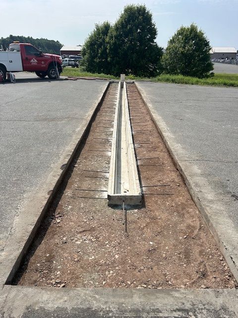 Concrete drainage channel being installed in a parking lot. Grey concrete with exposed aggregate. Brown dirt and a red truck.