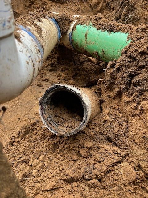 Pipes buried in dirt; white, green, and blue pipes connect. One white pipe is damaged.
