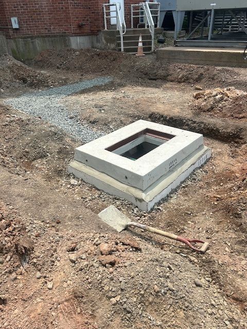 A rectangular concrete utility access point under construction outdoors with a shovel lying near.