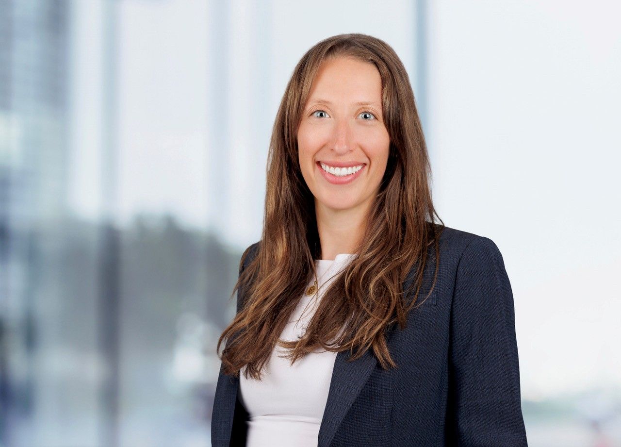Smiling woman in a dark blazer and white top against a bright office background