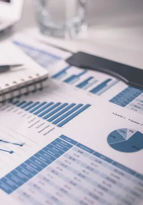 Financial charts and graphs, blue and white, with a notebook, pen, and phone, on a desk.