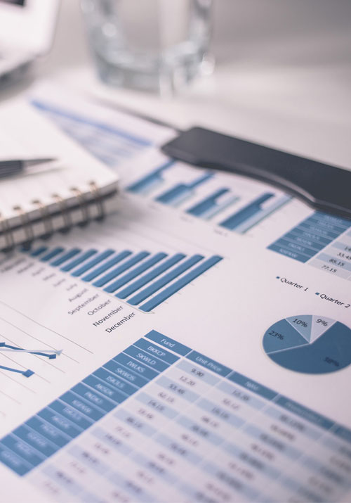 Financial charts and graphs, blue and white, with a notebook, pen, and phone, on a desk.