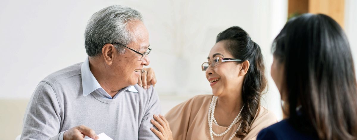 Older couple talking with a young woman, all wearing glasses and smiling, indoors.