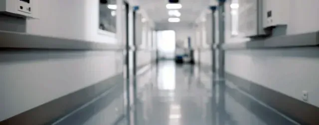 Hospital hallway with shiny floor, white walls, and bright overhead lights.