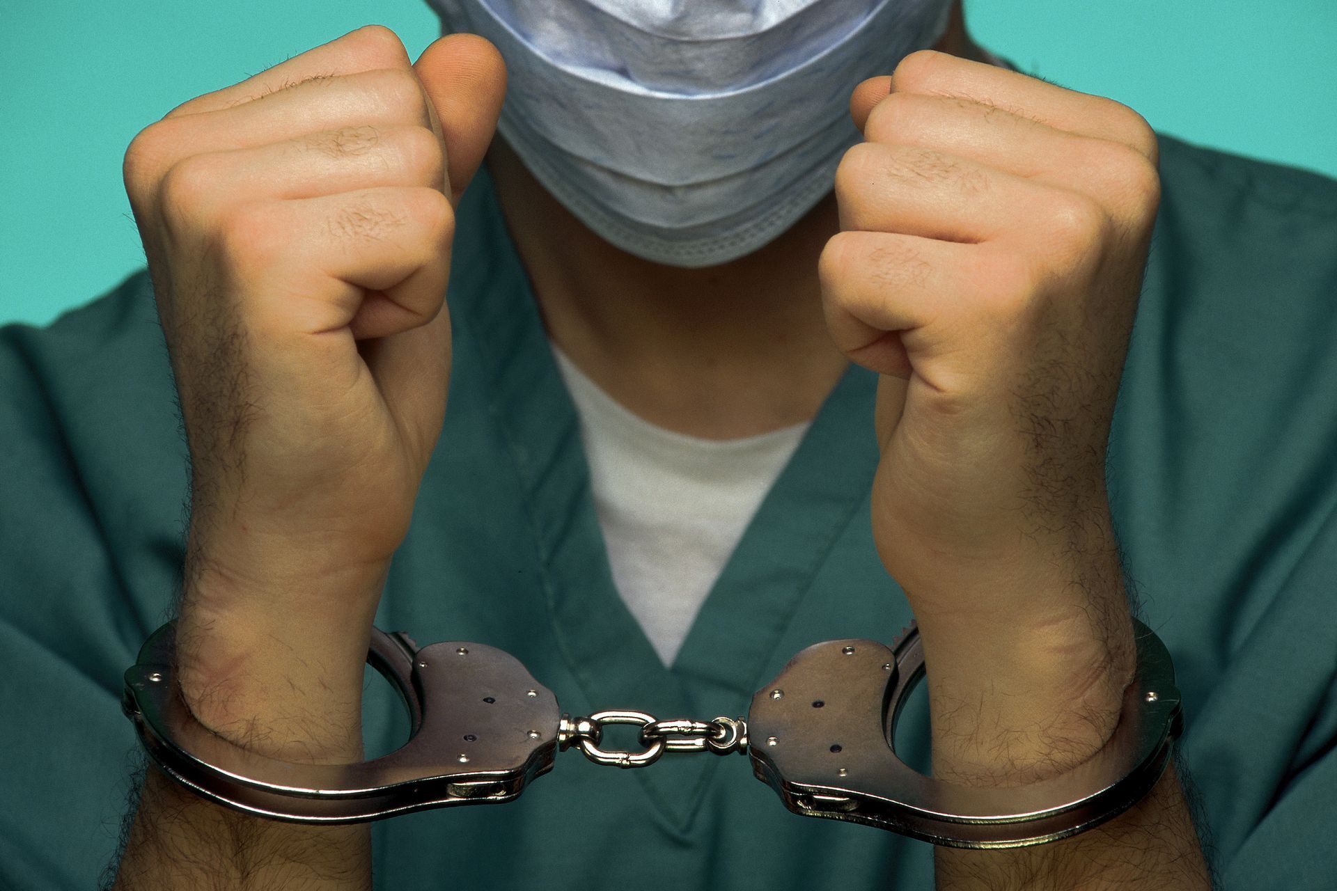 Doctor in surgical scrubs with hands cuffed in front.