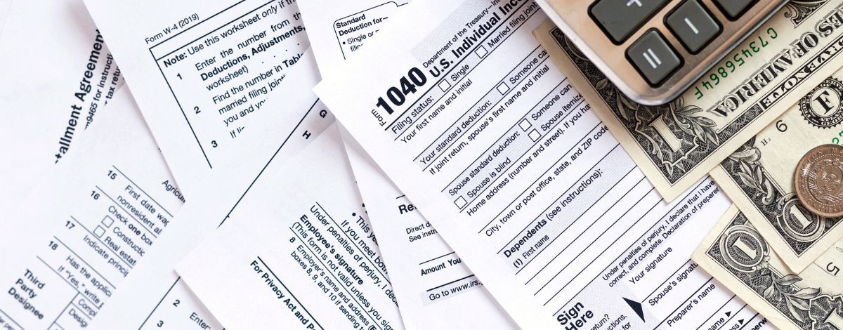 Tax forms, calculator, and money are displayed on a white surface.