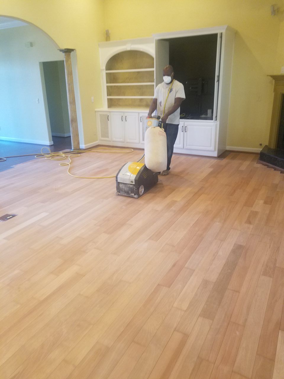 A man is sanding a wooden floor in a living room.