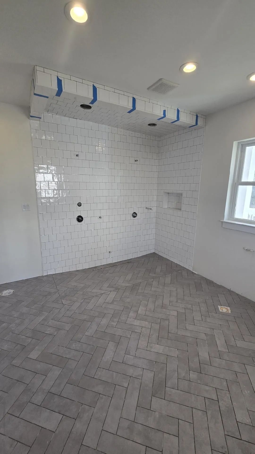 A bathroom with white tiles and a herringbone floor.