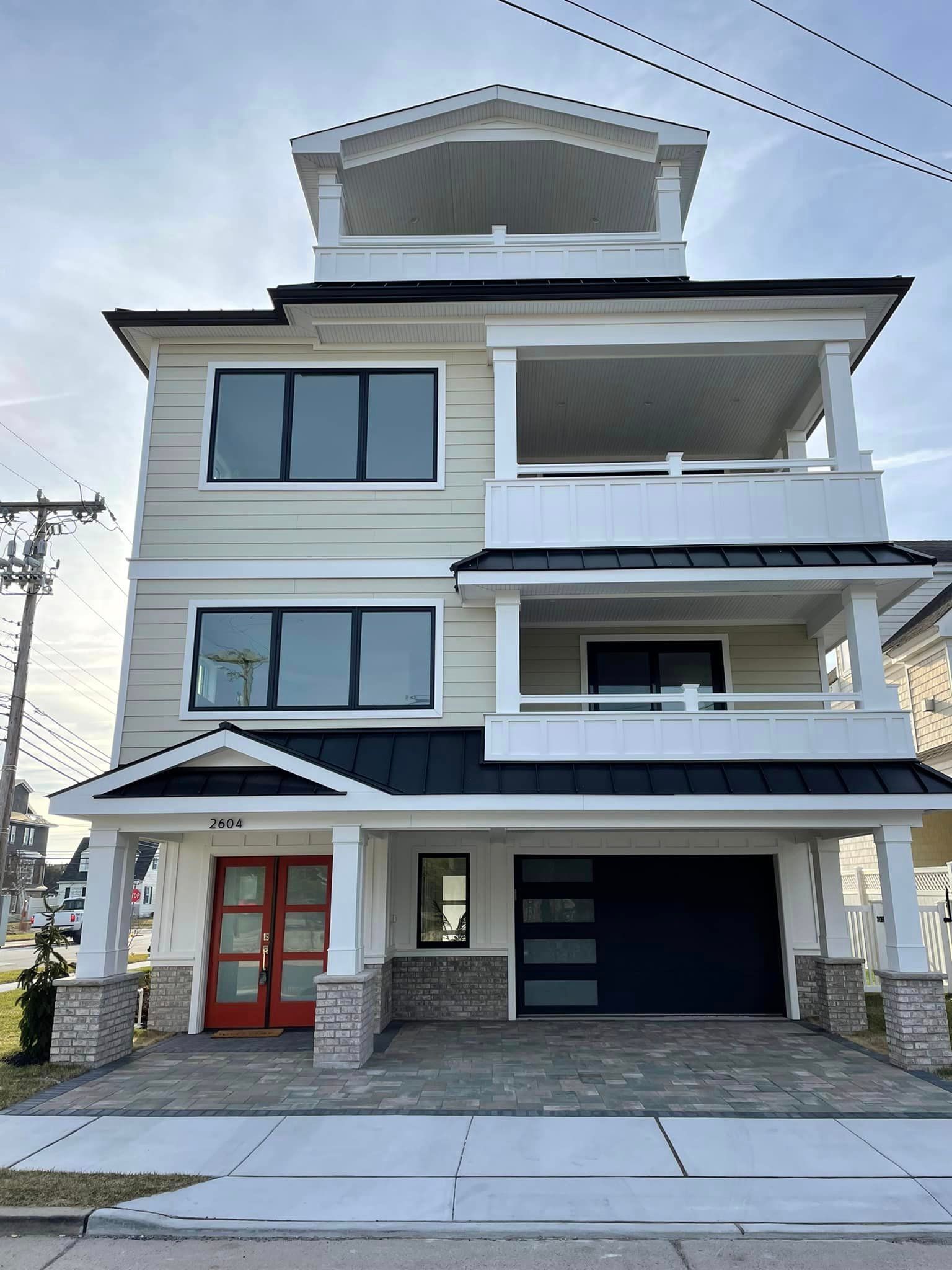 A large white house with a black garage and a red door.