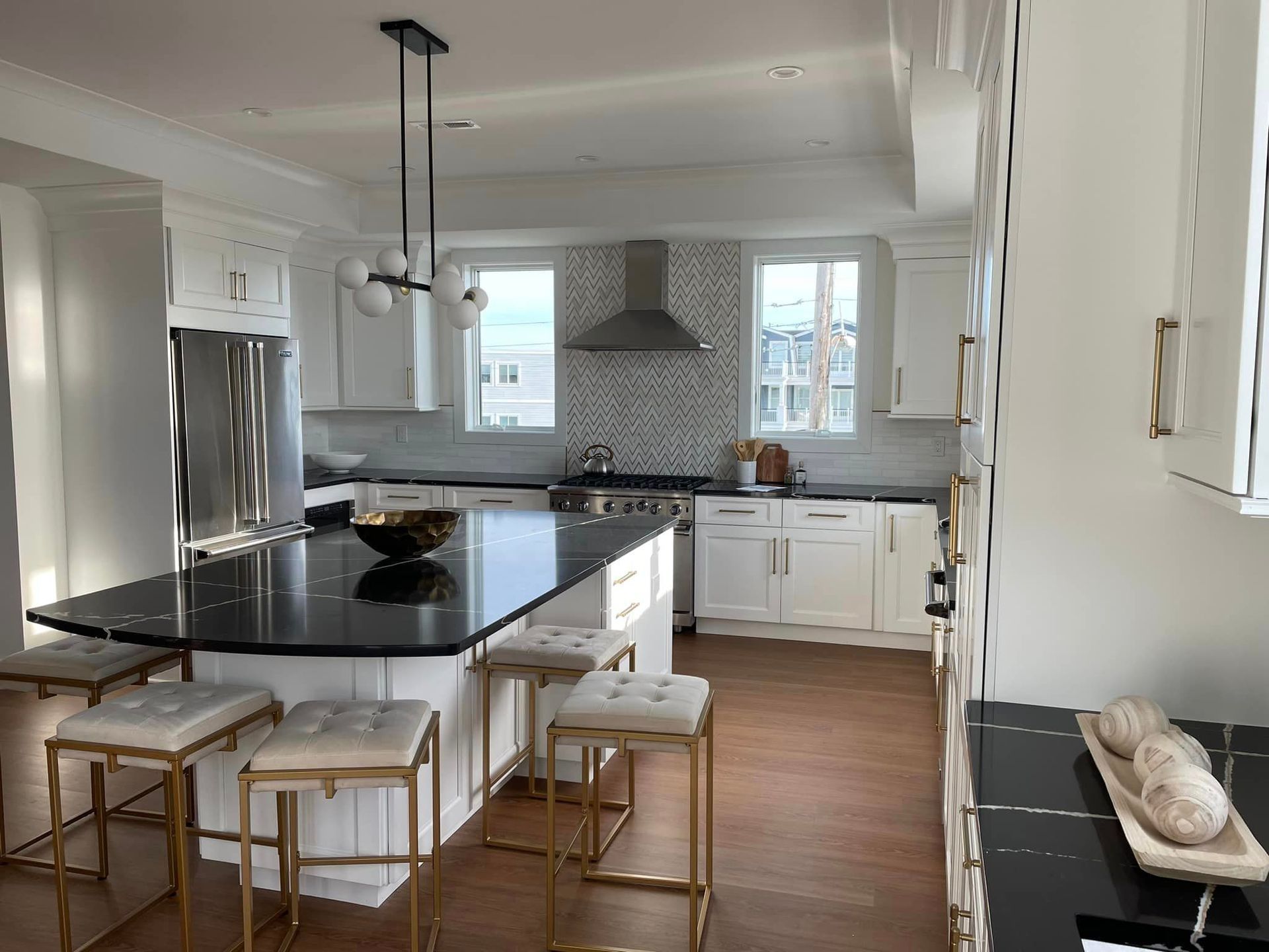 A kitchen with white cabinets, black counter tops, stools and a large island.