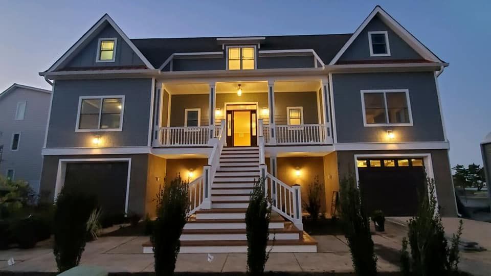 A large house with a large porch and stairs is lit up at night.
