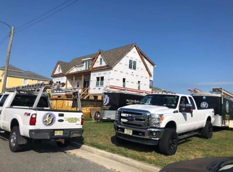 Two white trucks are parked in front of a house under construction.
