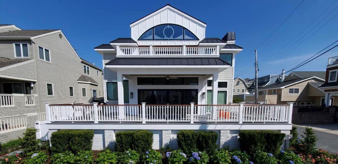 A large white house with a balcony is surrounded by other houses.