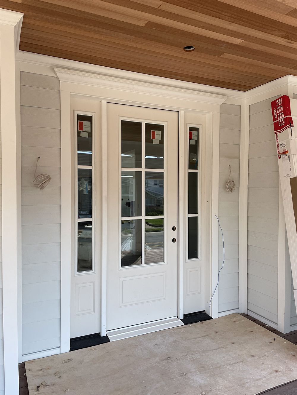 A white door with a wooden ceiling is sitting on a porch.