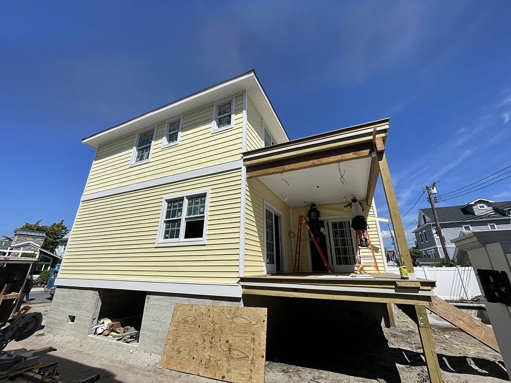 A yellow house with a porch is being remodeled