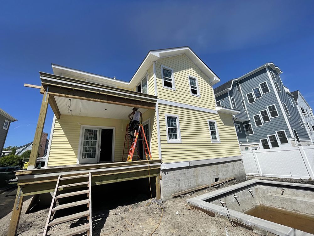 A man is standing on a ladder in front of a house under construction.