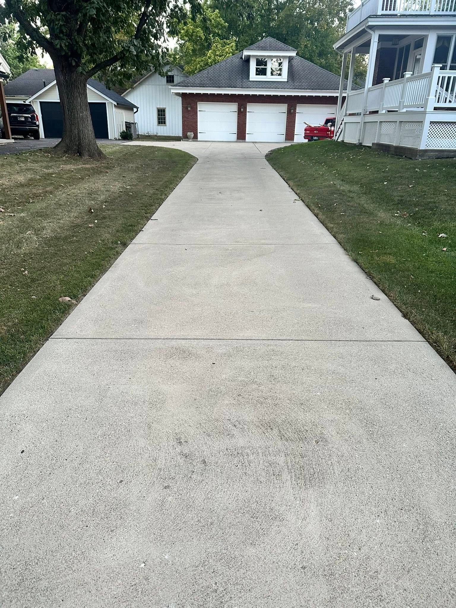 Long concrete driveway leading to a white house with a two-car garage and porch.