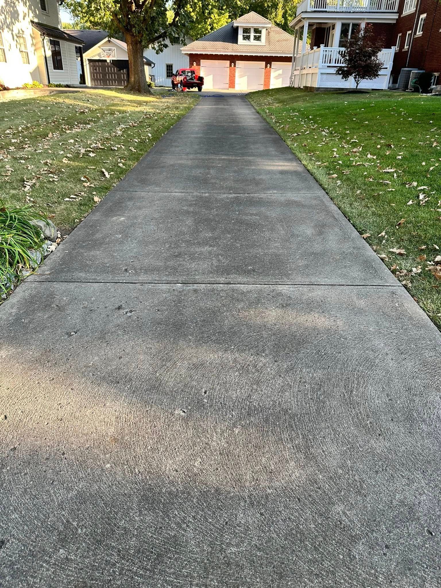 Concrete driveway leading to suburban houses with trees and patchy grass on either side