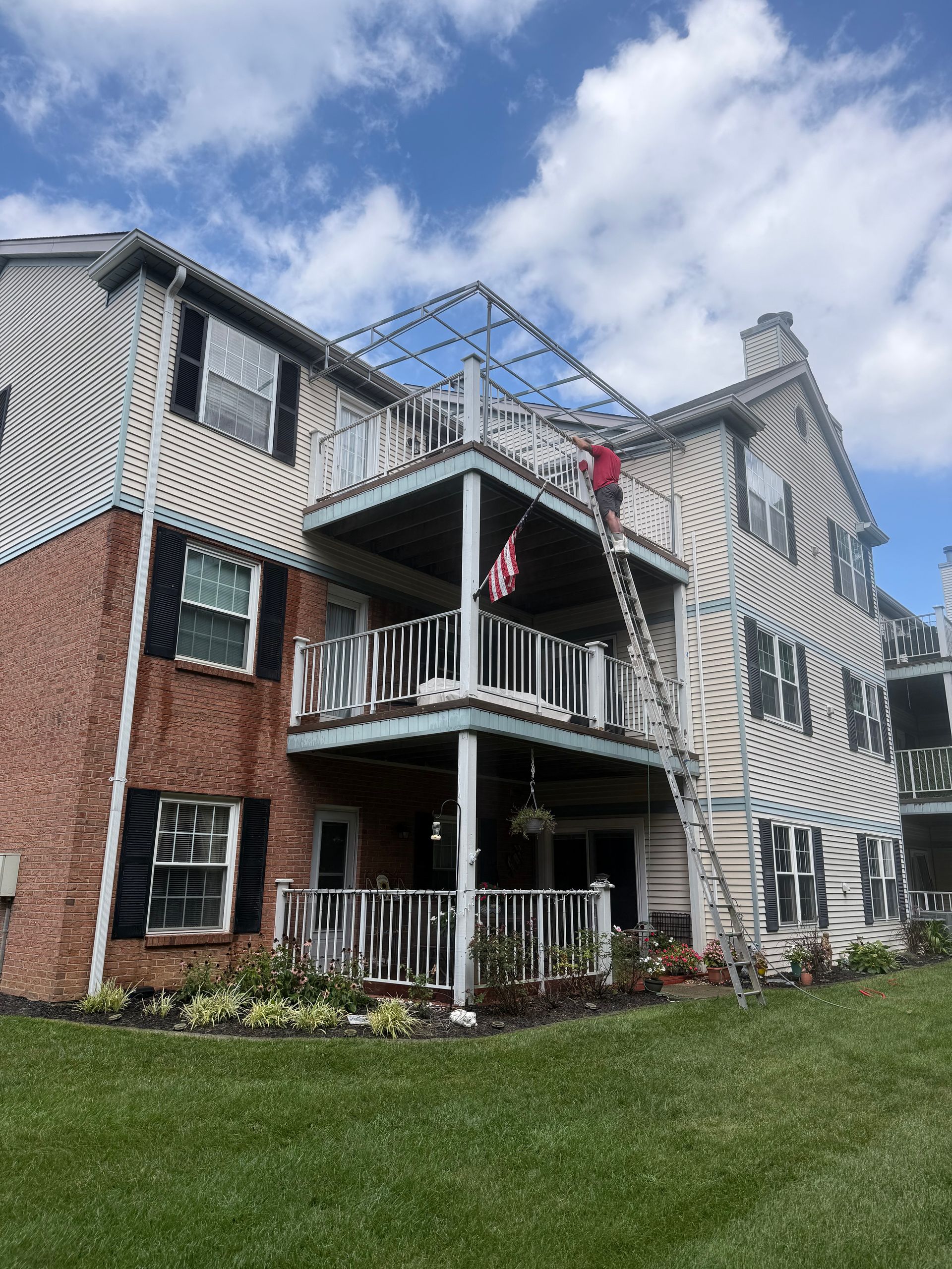 Three-story apartment building with brick and white siding, balconies, and an American flag under a cloudy sky
