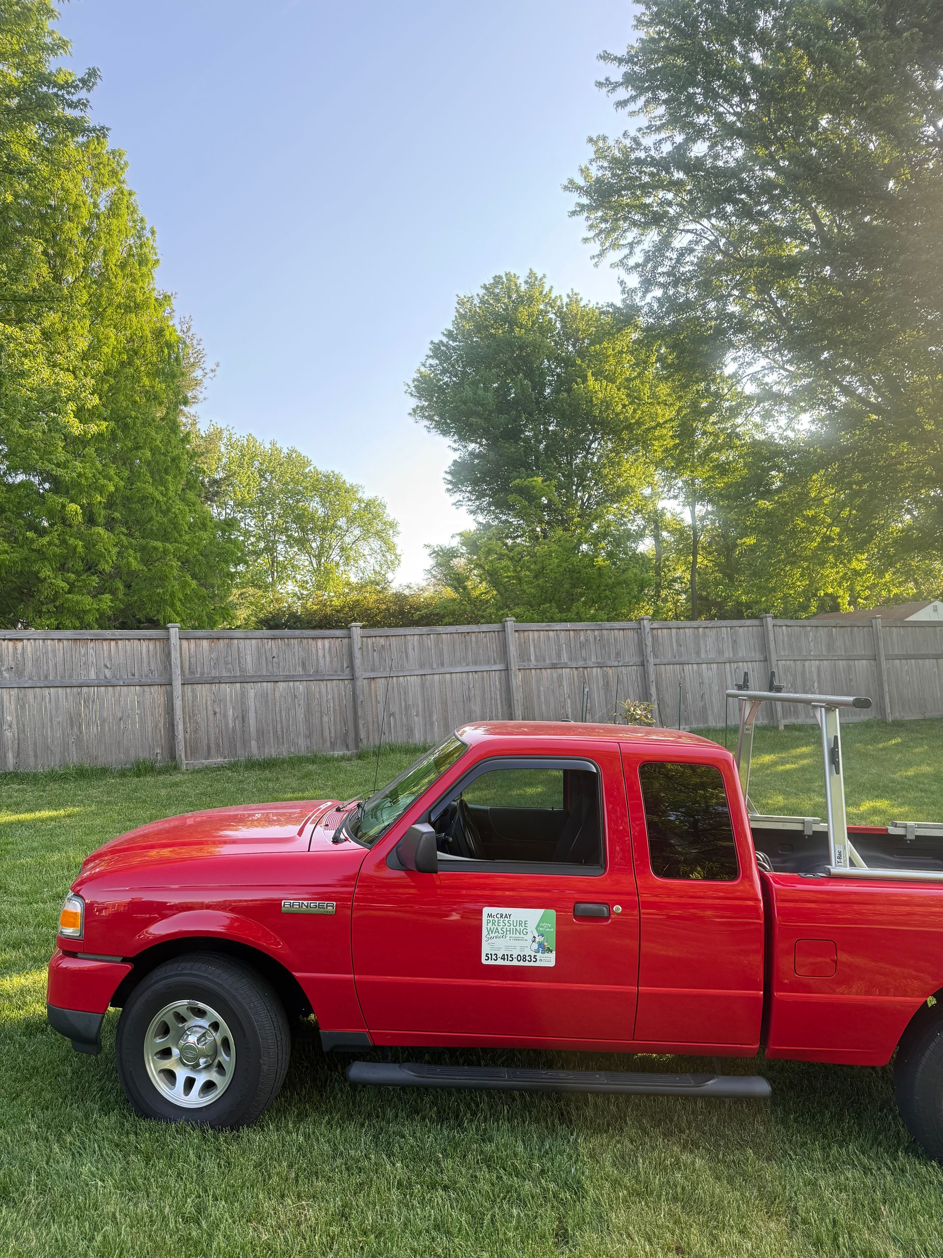 Red pickup truck parked by a wooden fence under tall green trees