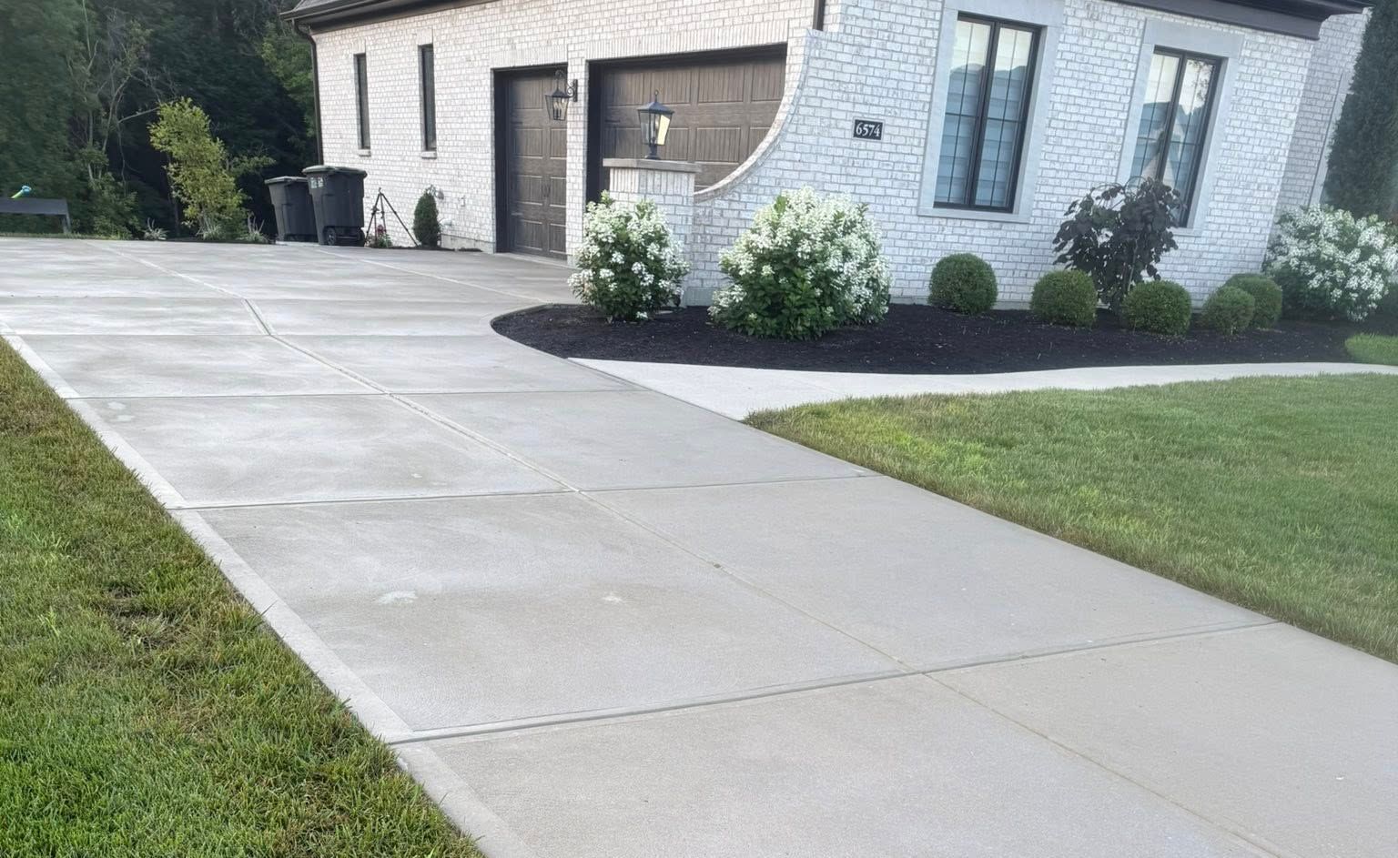 Concrete driveway leading to a white house with a neatly edged lawn and shrubs