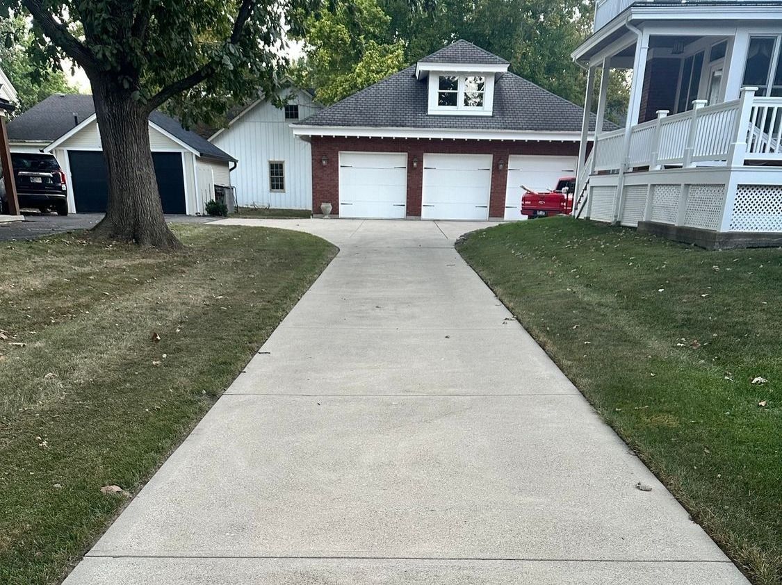 Concrete driveway leading to a white garage with red doors in a suburban yard