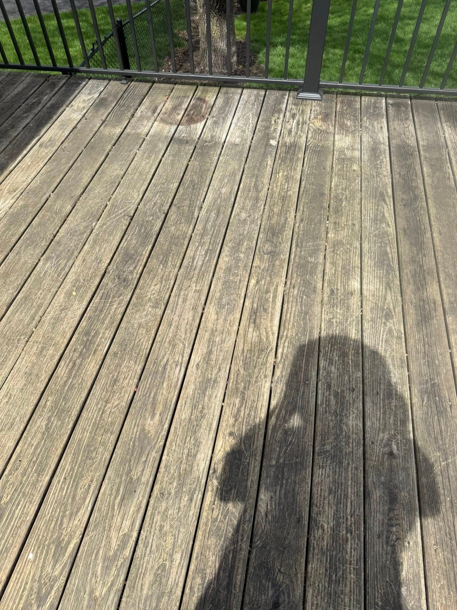 Sunlit wooden deck with railing and a person’s shadow in the foreground