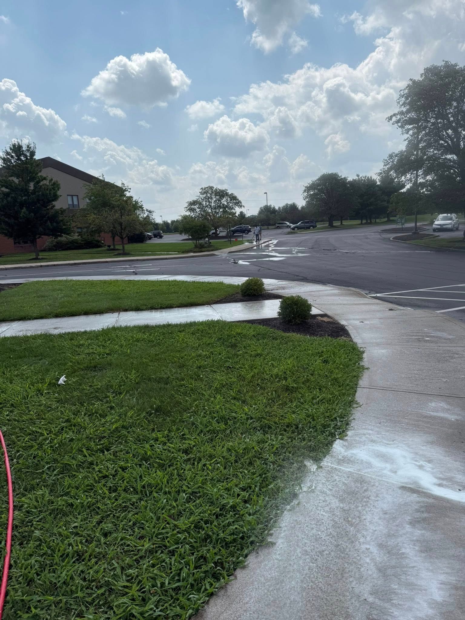 Wet suburban parking lot beside green lawn under a cloudy sky