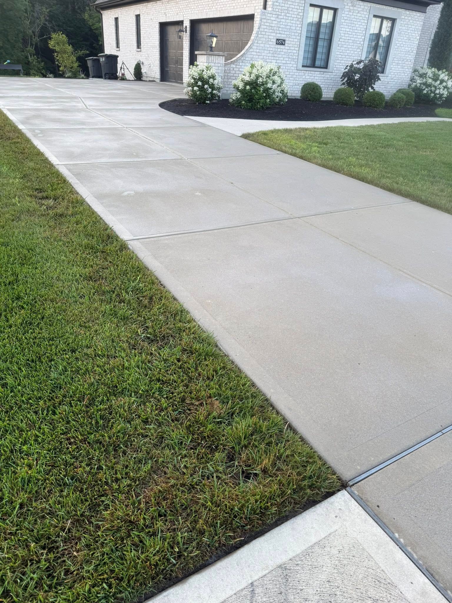 Concrete driveway leading to a modern house with green lawn and shrubs