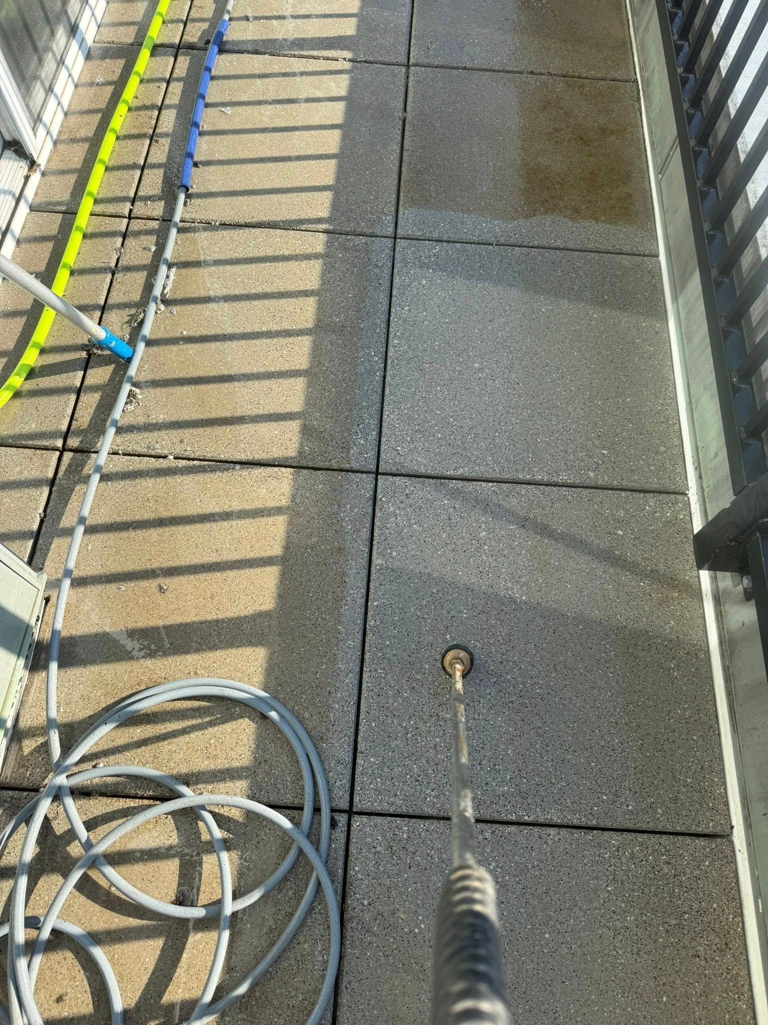 Narrow concrete walkway with metal railings, coiled cable, and a rope on the ground in sunlight