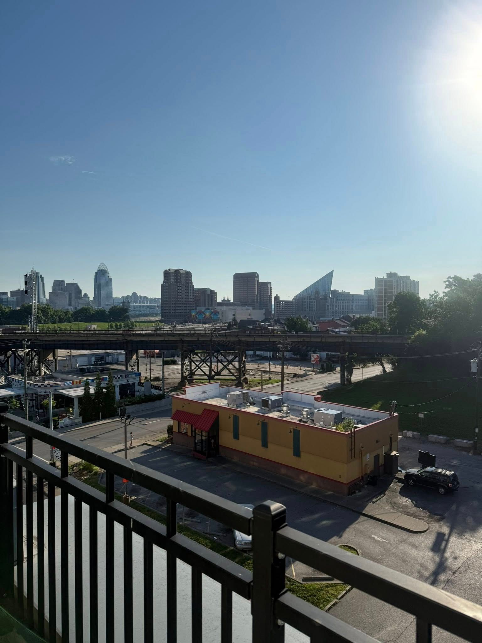 Sunlit city skyline beyond rail tracks, with a fence in foreground and small buildings below