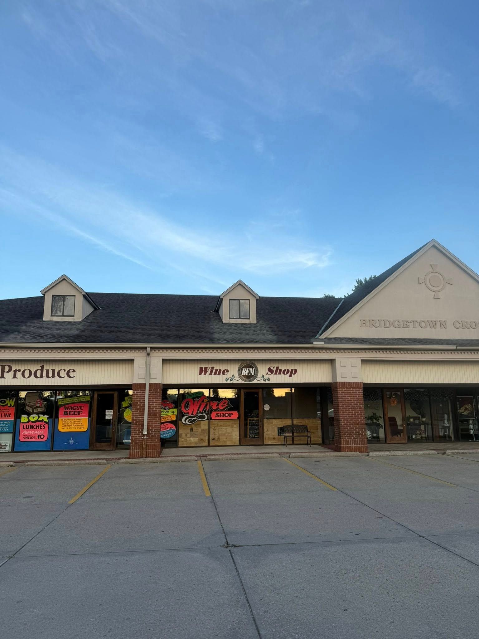 Strip mall storefronts with signs, brick columns, and a blue sky overhead