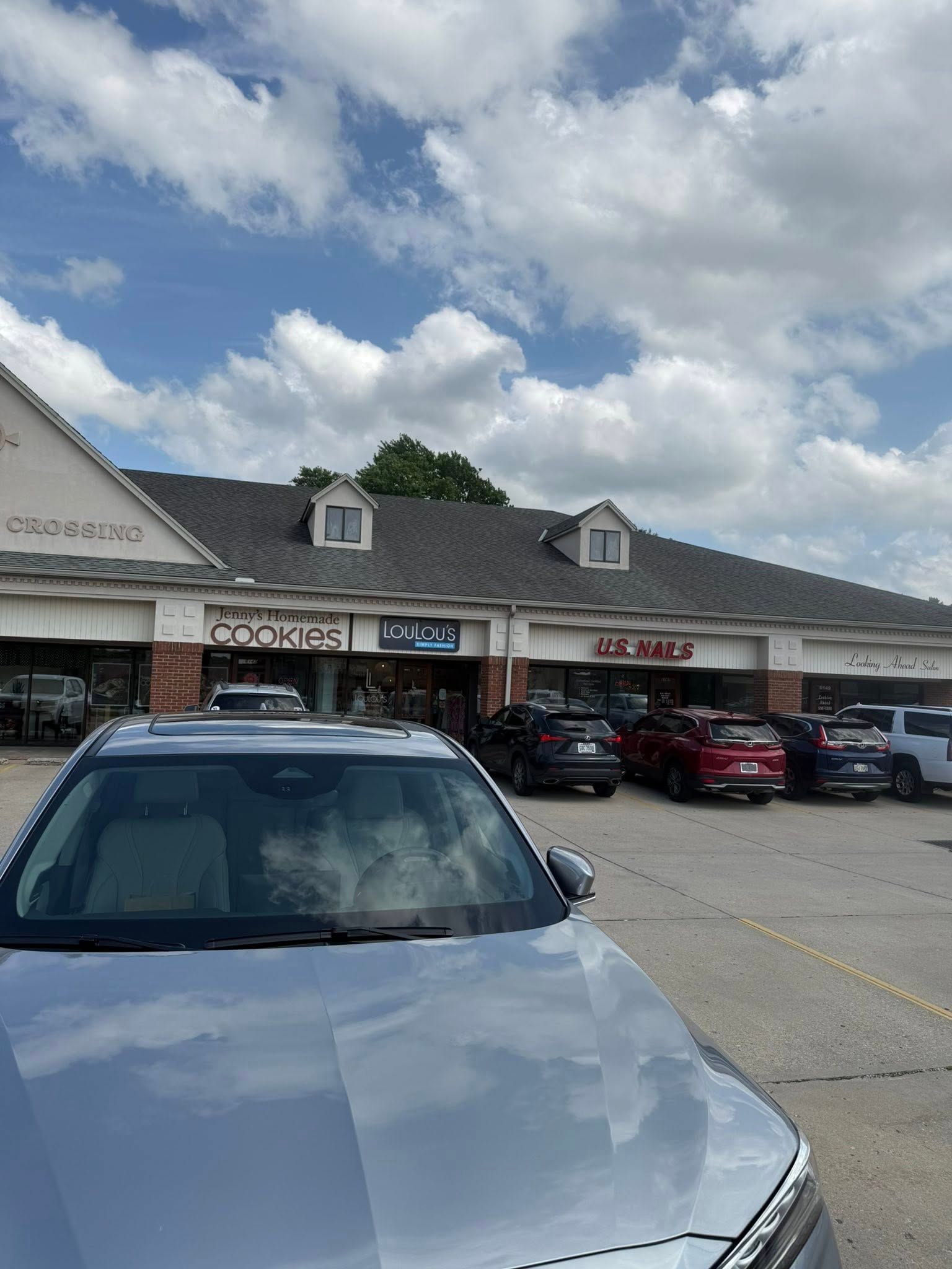 Shopping plaza parking lot with a silver car in front of storefronts under a cloudy sky