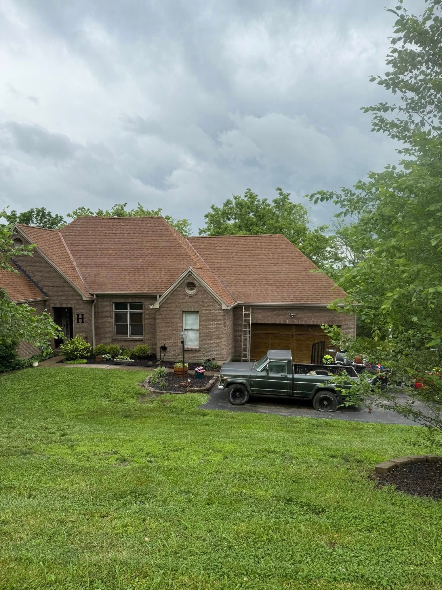 Brick house with red-tiled roof, green lawn, and pickup truck under cloudy sky