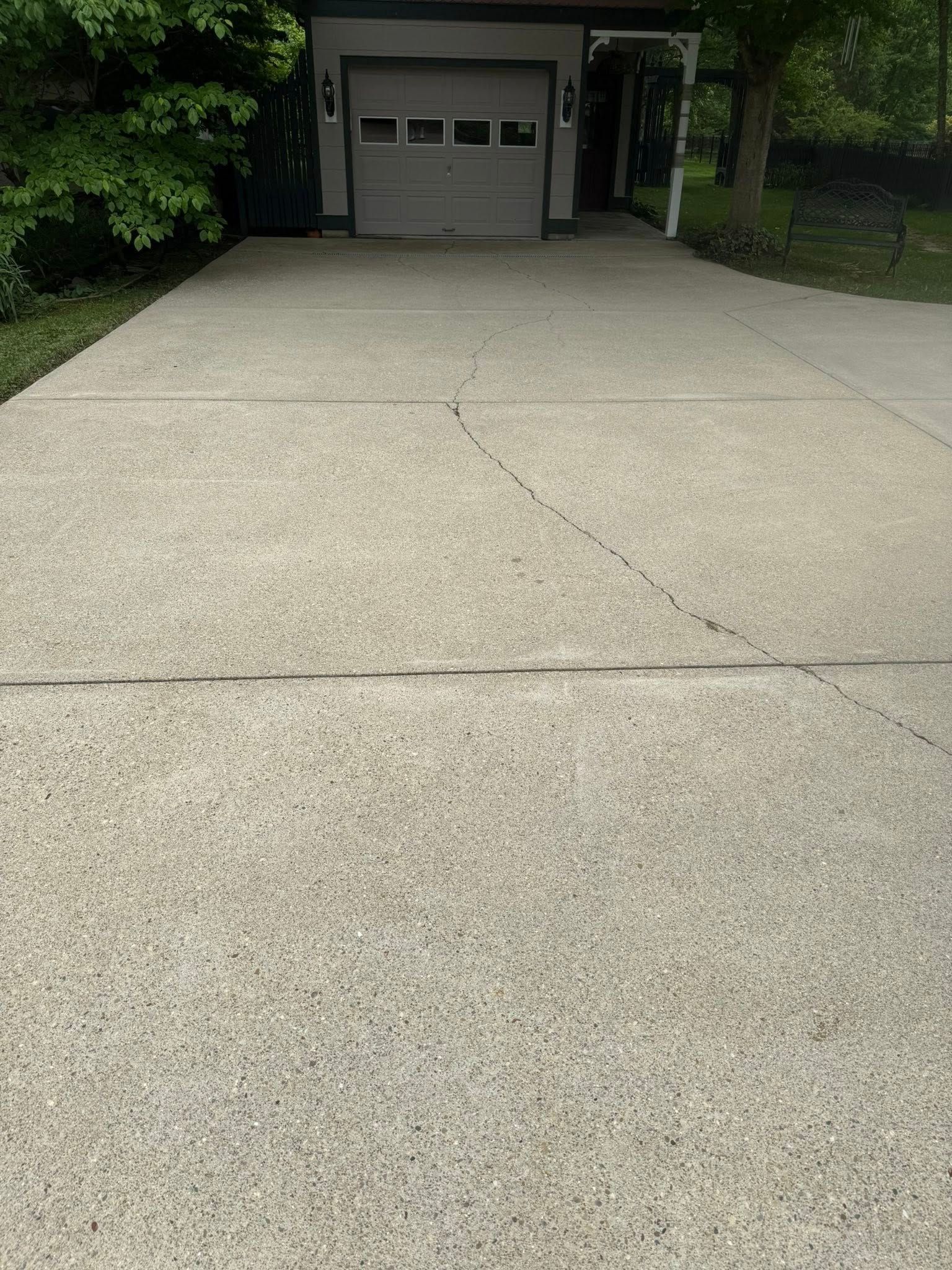 Concrete driveway leading to a garage with a closed door, bordered by trees and grass.