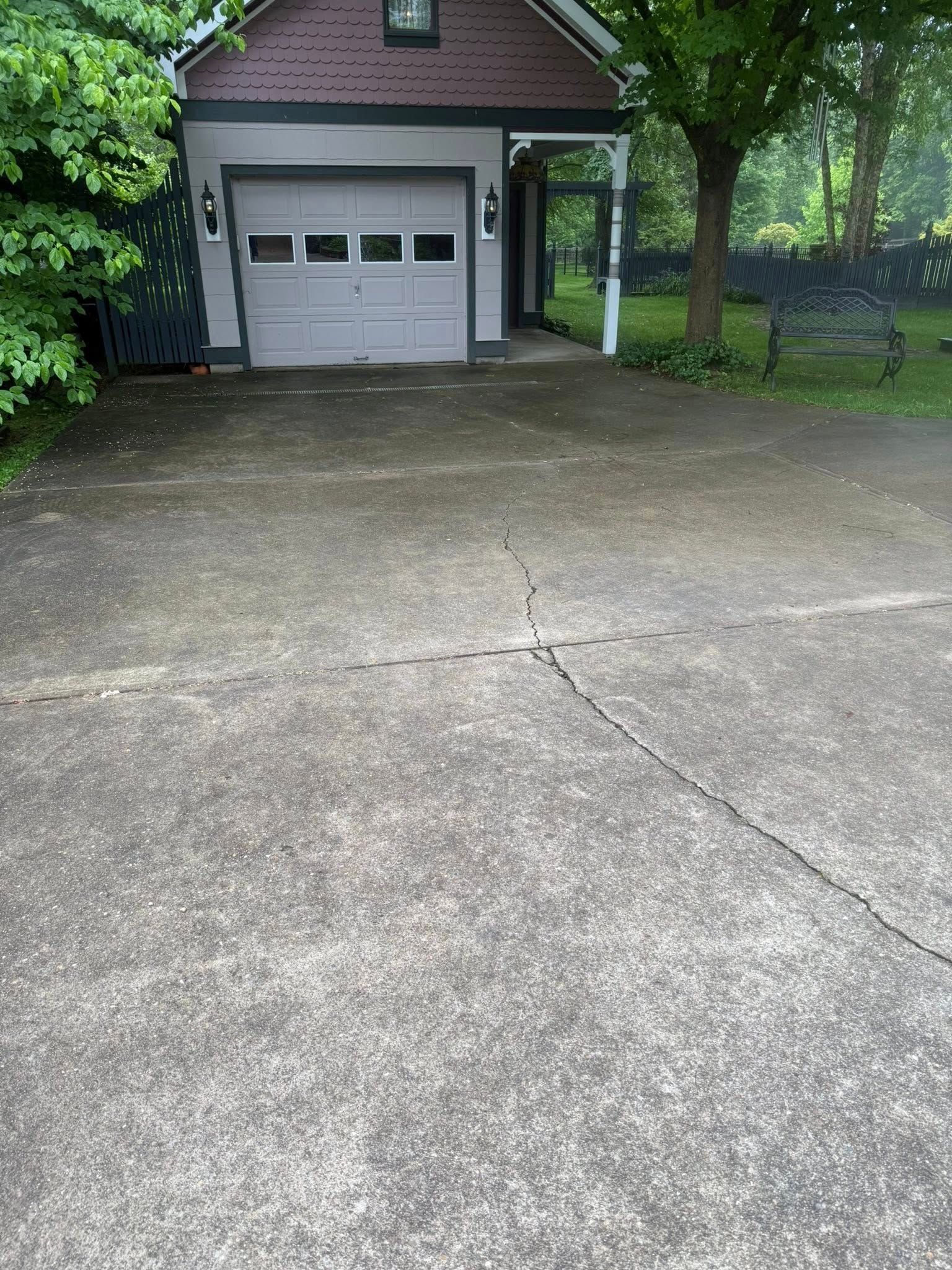 Concrete driveway leading to a garage with a brick house and green trees on either side.