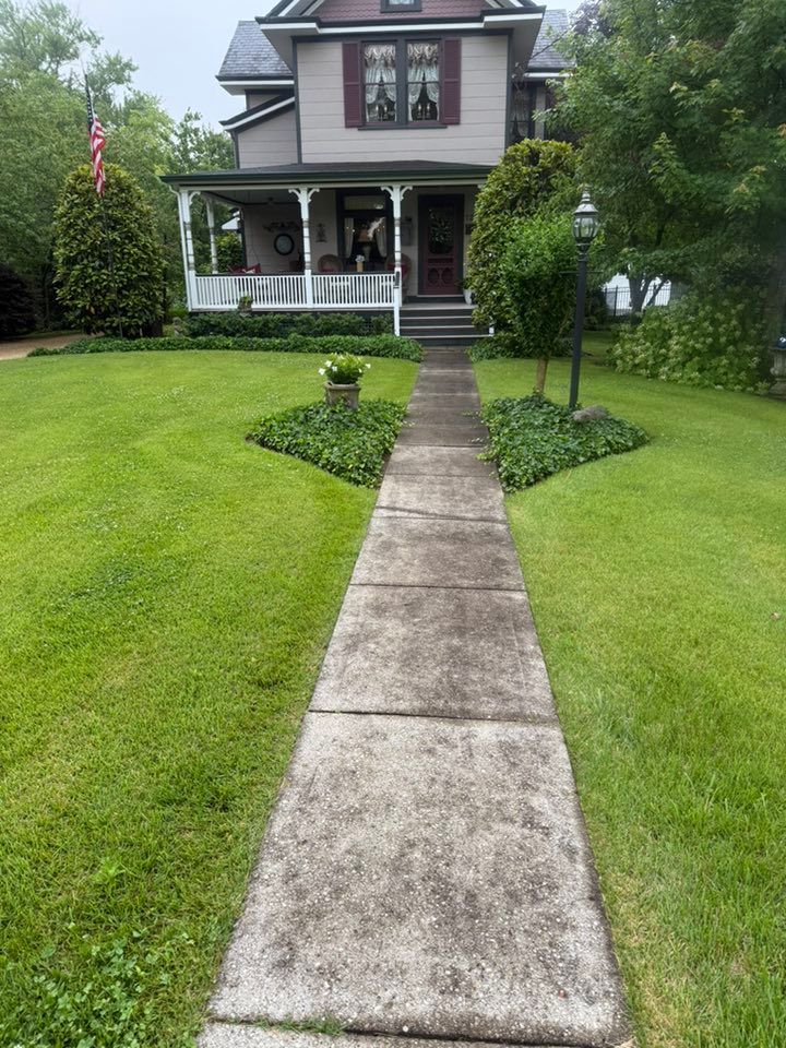 Two-story house with a front porch and a concrete walkway through a green lawn.