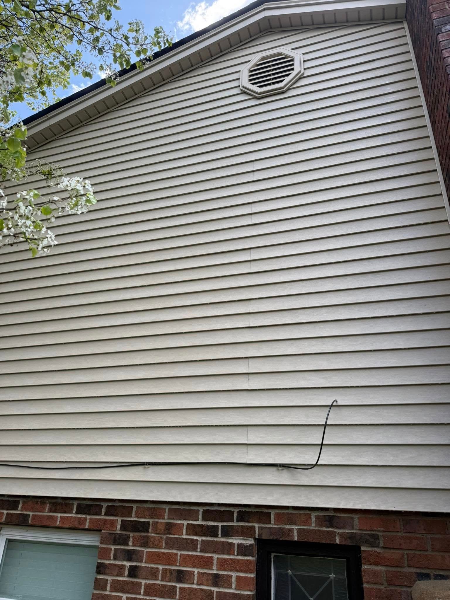 House exterior with gray siding, brick foundation, and a small circular vent near the roofline