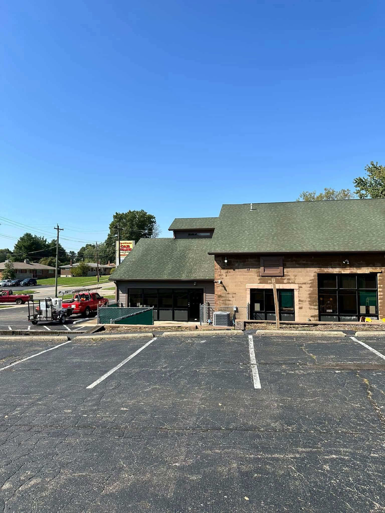 Empty parking lot in front of a small brick-and-green building under a clear blue sky