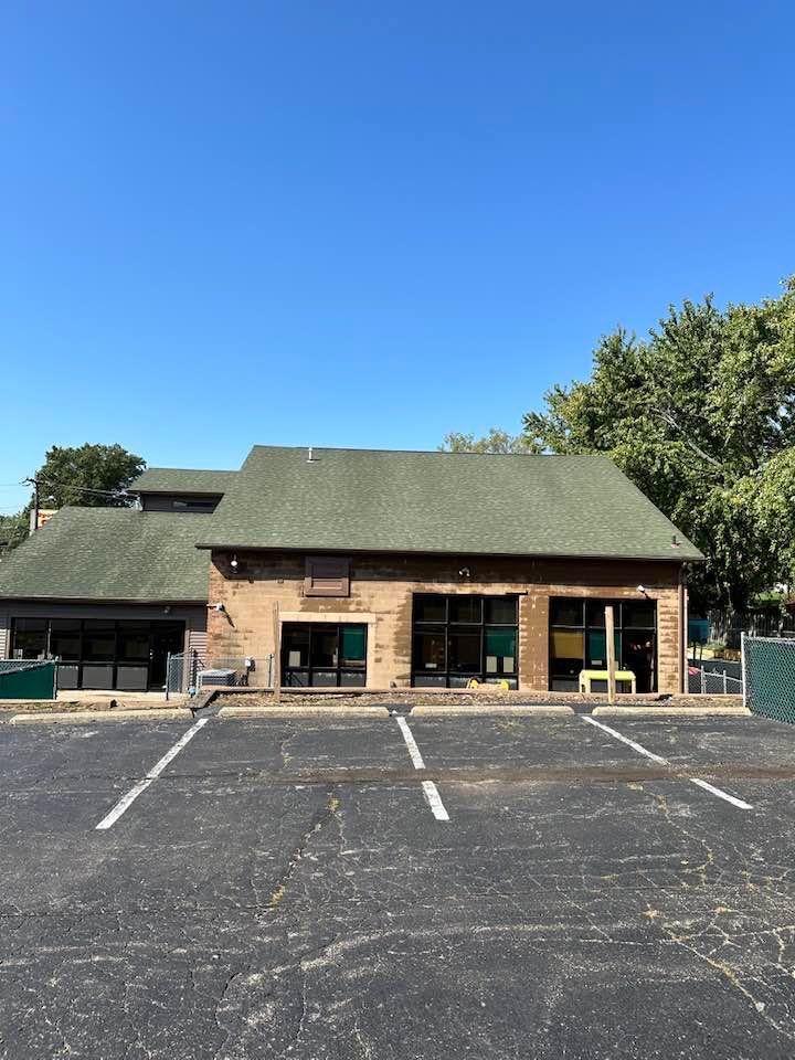 Brick building with green roof and empty parking lot under a clear blue sky