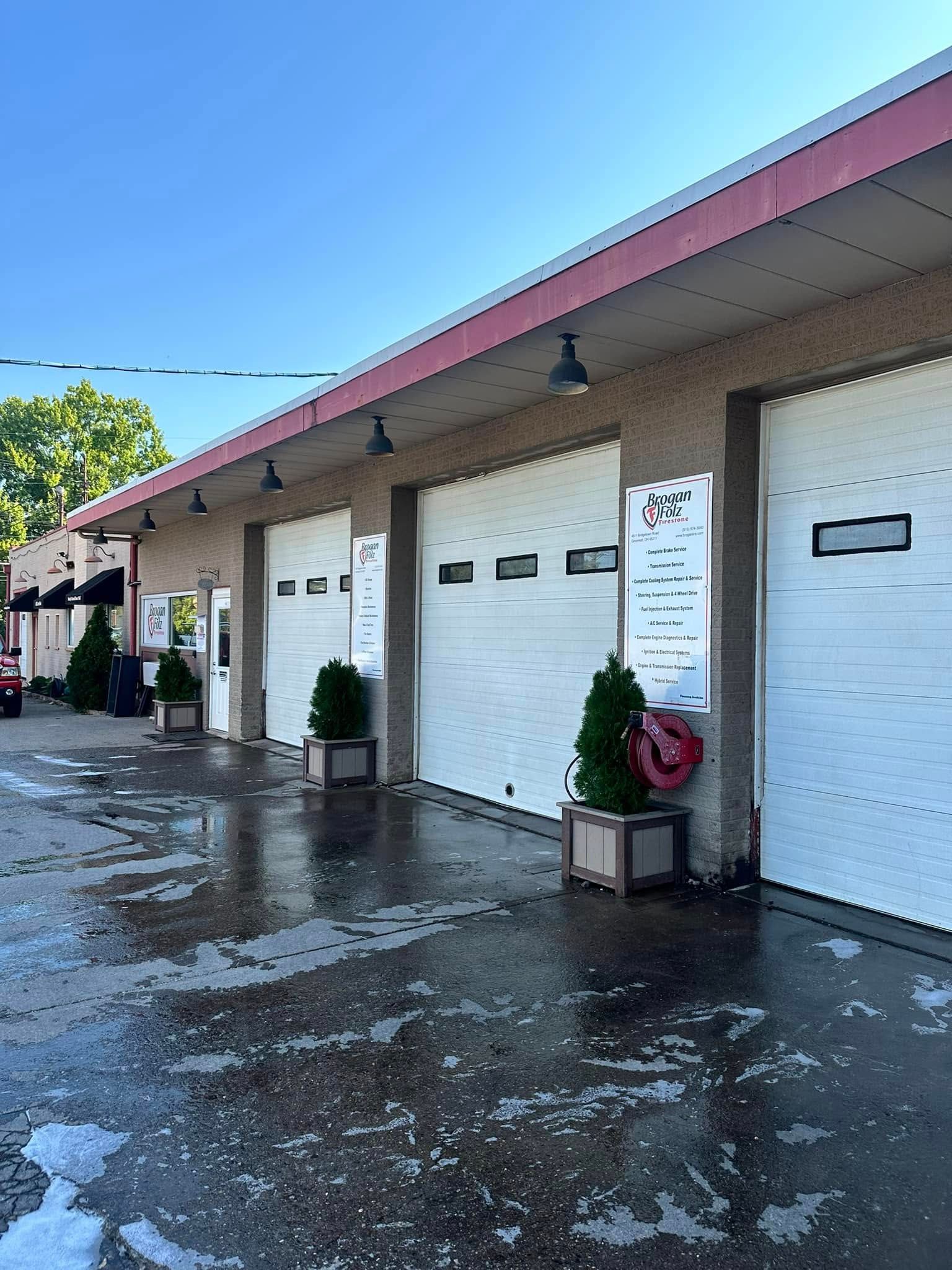 Row of white garage doors under a maroon roof, with wet pavement and potted plants along the building