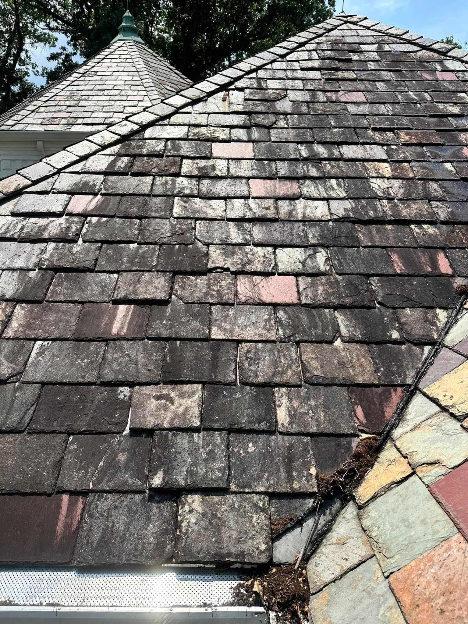 Weathered shingle roof with visible wear, moss stains, and a small section of multicolored tiles