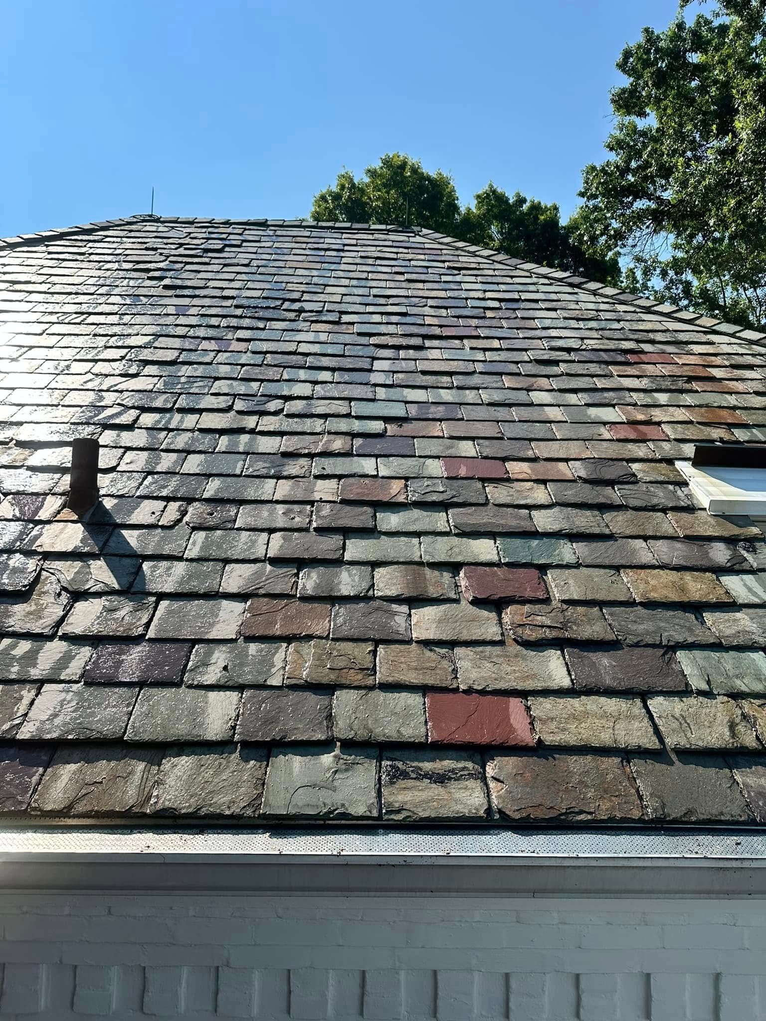 Weathered shingle roof with a black gutter, seen against a blue sky and trees