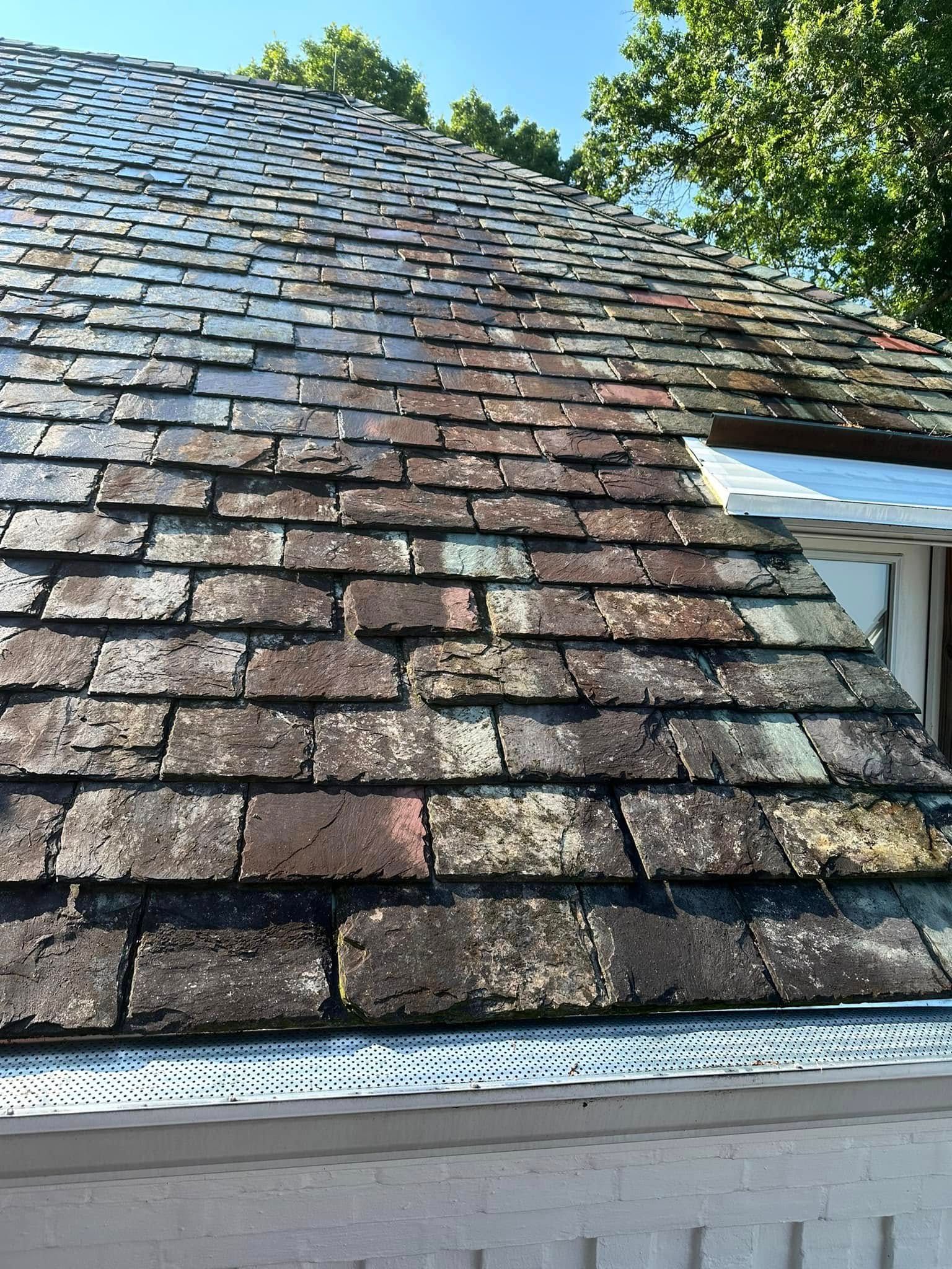 Weathered shingle roof with a dormer window and white gutters under a blue sky