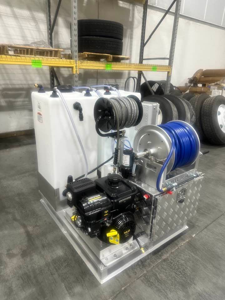 Industrial hose reel setup with black pump, blue hose, and white tanks on a metal frame in a warehouse